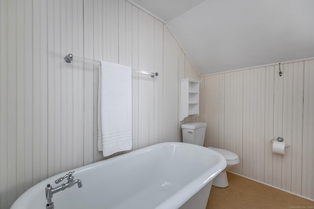 bathroom featuring lofted ceiling, a soaking tub, toilet, and wooden walls