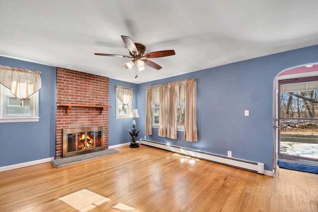 unfurnished living room with a baseboard radiator, a healthy amount of sunlight, hardwood / wood-style floors, and a fireplace