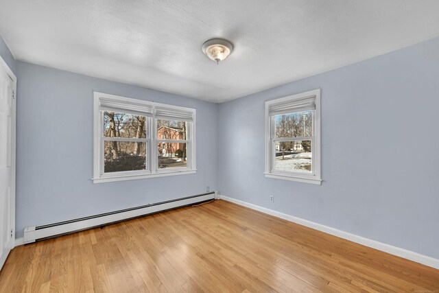 unfurnished room featuring a wealth of natural light, light hardwood / wood-style floors, and baseboard heating