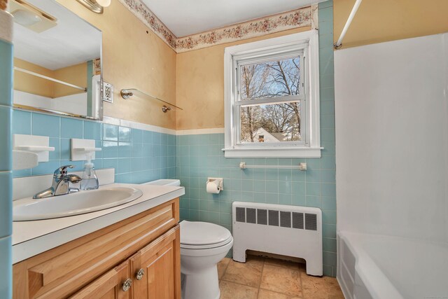 full bathroom with radiator, tile walls, tile patterned flooring, vanity, and toilet