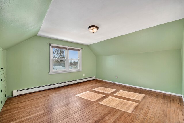 additional living space featuring lofted ceiling, light hardwood / wood-style floors, and a baseboard heating unit