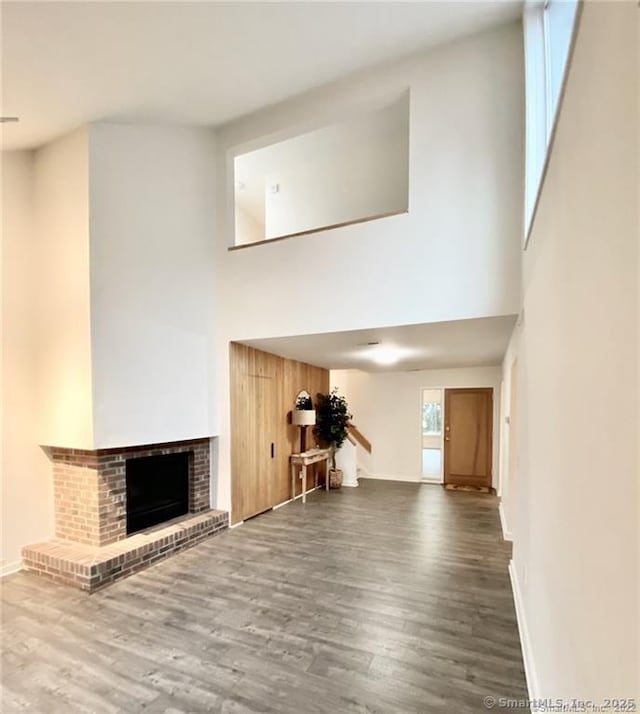 unfurnished living room featuring hardwood / wood-style floors, a brick fireplace, and a high ceiling