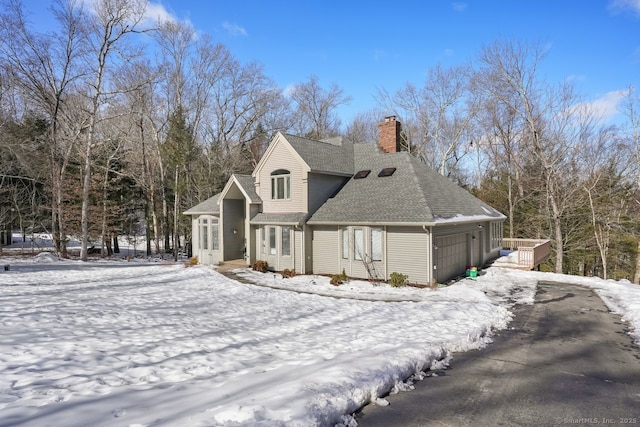 view of front facade featuring driveway, a chimney, a garage, and roof with shingles