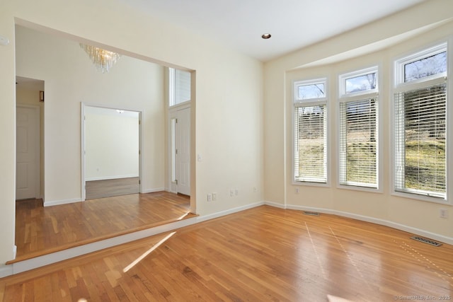 spare room with light wood-style flooring, baseboards, visible vents, and a chandelier