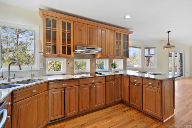 kitchen with a peninsula, brown cabinetry, under cabinet range hood, and a sink