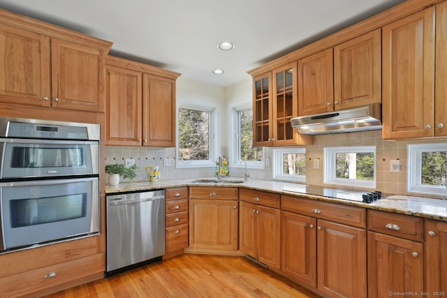 kitchen featuring light stone counters, brown cabinetry, a sink, appliances with stainless steel finishes, and under cabinet range hood