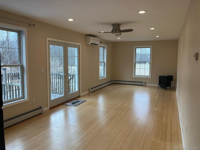 empty room with a wood stove, a wall mounted AC, a baseboard heating unit, light wood-type flooring, and french doors