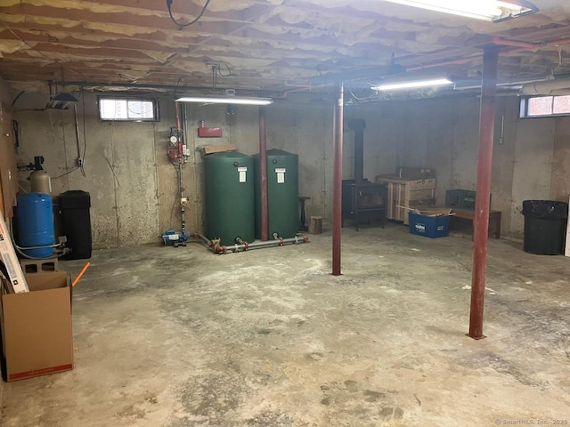 basement featuring a healthy amount of sunlight, water heater, and a wood stove