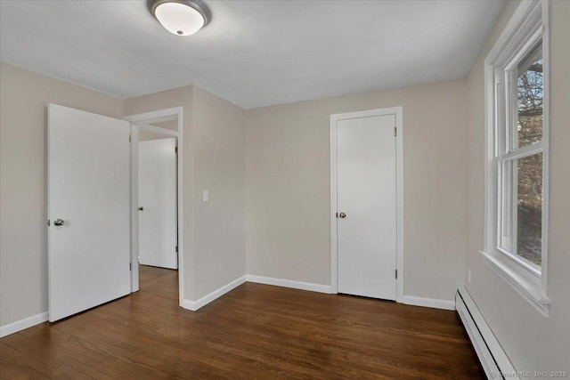 unfurnished bedroom featuring a baseboard heating unit and dark wood-type flooring