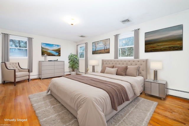 bedroom with multiple windows, baseboard heating, and light hardwood / wood-style floors