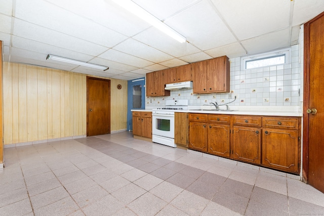 kitchen featuring sink, white gas range oven, wooden walls, a drop ceiling, and decorative backsplash