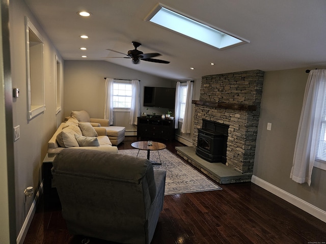 living room with dark wood-type flooring, a wood stove, vaulted ceiling with skylight, and baseboard heating