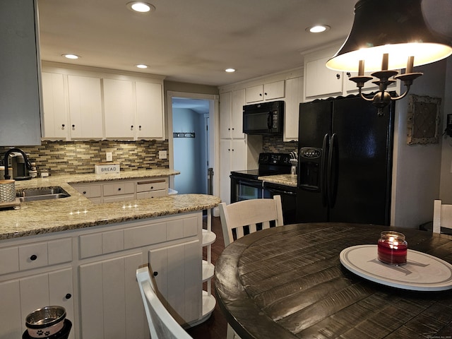 kitchen with sink, white cabinetry, light stone counters, hanging light fixtures, and black appliances