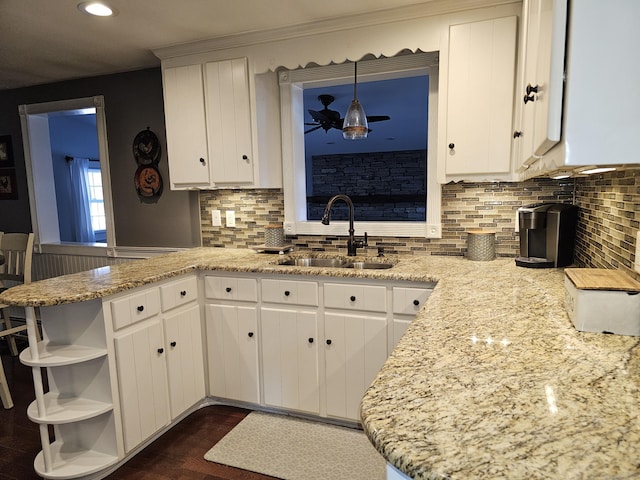 kitchen with sink, light stone counters, decorative light fixtures, kitchen peninsula, and white cabinets