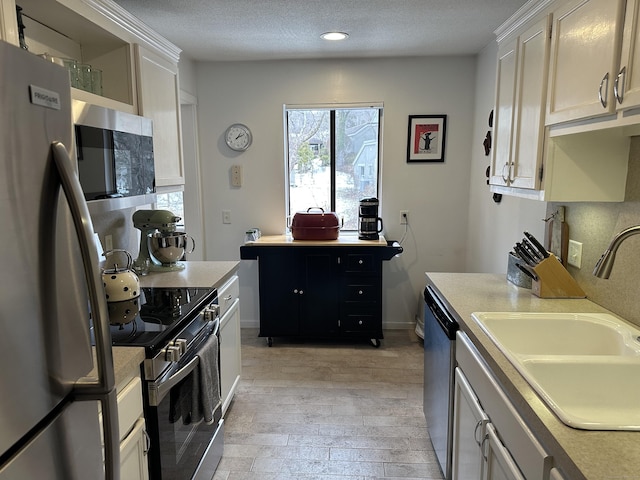 kitchen featuring sink, white cabinetry, a textured ceiling, light wood-type flooring, and appliances with stainless steel finishes