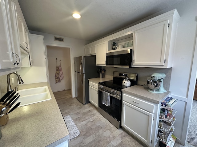 kitchen featuring appliances with stainless steel finishes, white cabinets, visible vents, and a sink