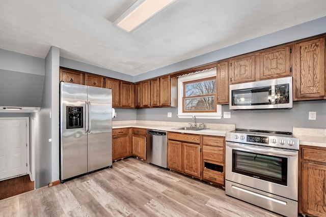 kitchen with appliances with stainless steel finishes, sink, and light wood-type flooring