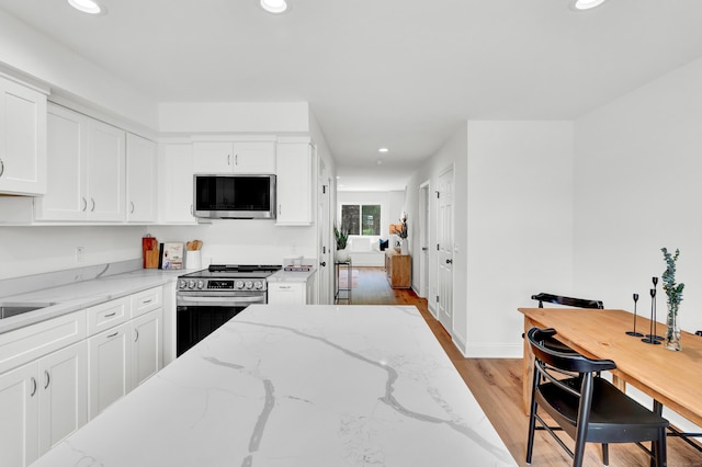 kitchen with appliances with stainless steel finishes, light stone countertops, light hardwood / wood-style floors, and white cabinets