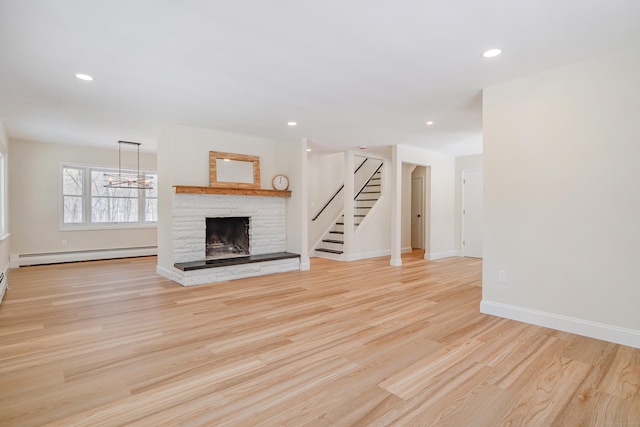 unfurnished living room with a notable chandelier, a baseboard heating unit, a stone fireplace, and light hardwood / wood-style floors