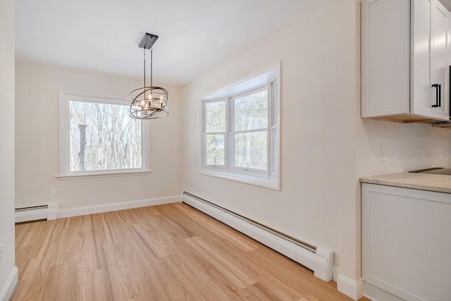 unfurnished dining area featuring an inviting chandelier, a baseboard heating unit, and light hardwood / wood-style flooring