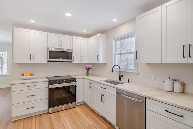 kitchen with sink, light hardwood / wood-style flooring, stainless steel appliances, light stone countertops, and white cabinets