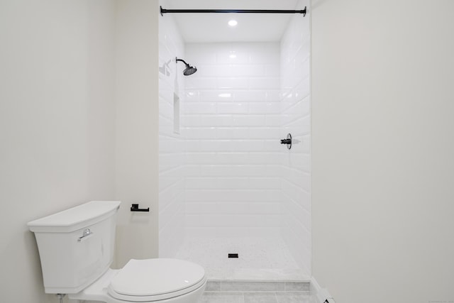 bathroom with tile patterned flooring, tiled shower, and toilet