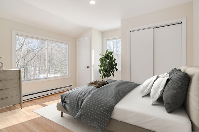 bedroom with baseboard heating, a closet, lofted ceiling, and light hardwood / wood-style flooring