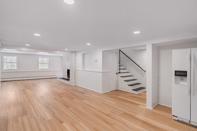 basement featuring a fireplace, light hardwood / wood-style flooring, white fridge with ice dispenser, and baseboard heating