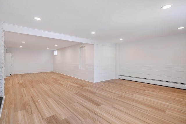 basement with white fridge, baseboard heating, and light hardwood / wood-style flooring