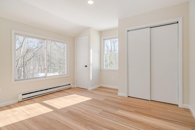 unfurnished bedroom with a closet, vaulted ceiling, light hardwood / wood-style flooring, and a baseboard heating unit