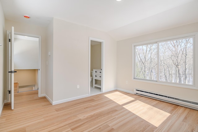 empty room featuring lofted ceiling, a baseboard heating unit, and light hardwood / wood-style floors