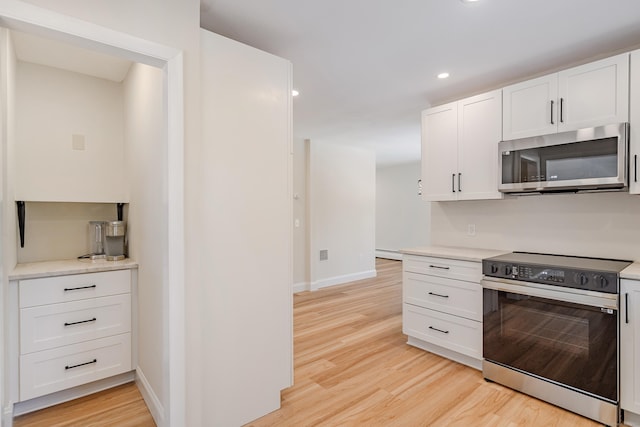 kitchen with stainless steel appliances, a baseboard heating unit, white cabinets, and light wood-type flooring