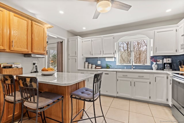 kitchen featuring electric stove, sink, a breakfast bar, dishwasher, and white cabinetry