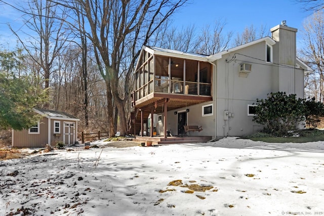 snow covered rear of property with a storage shed, a sunroom, and an AC wall unit