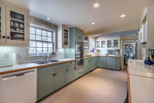 kitchen featuring white microwave, dishwashing machine, green cabinets, and a sink