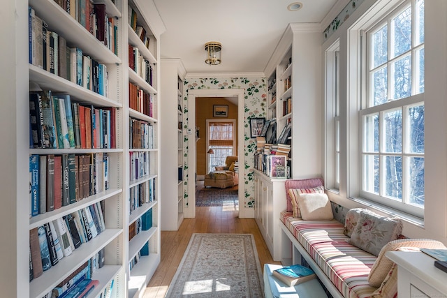 living area with wallpapered walls, crown molding, bookshelves, and light wood-type flooring