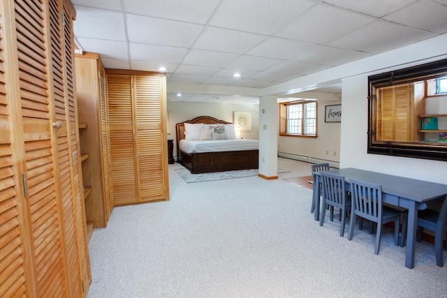 carpeted bedroom featuring a drop ceiling and a baseboard heating unit