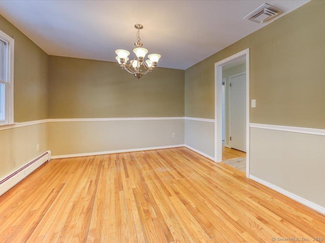 spare room with a baseboard heating unit, a chandelier, and light hardwood / wood-style floors