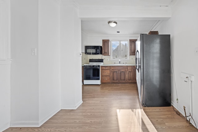 kitchen featuring stainless steel refrigerator, decorative backsplash, ornamental molding, gas range gas stove, and light wood-type flooring