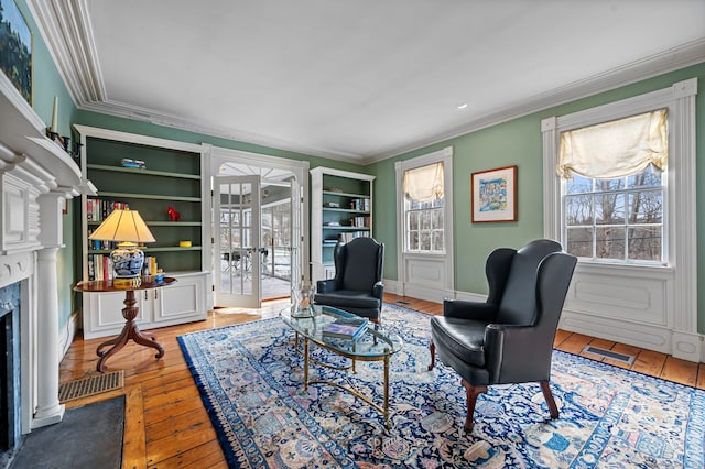 sitting room featuring hardwood / wood-style floors, crown molding, a high end fireplace, and french doors