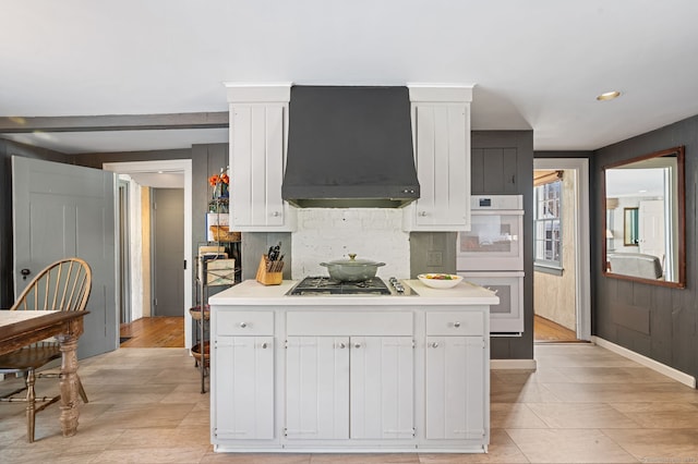 kitchen featuring premium range hood, white cabinetry, double oven, backsplash, and stainless steel gas cooktop