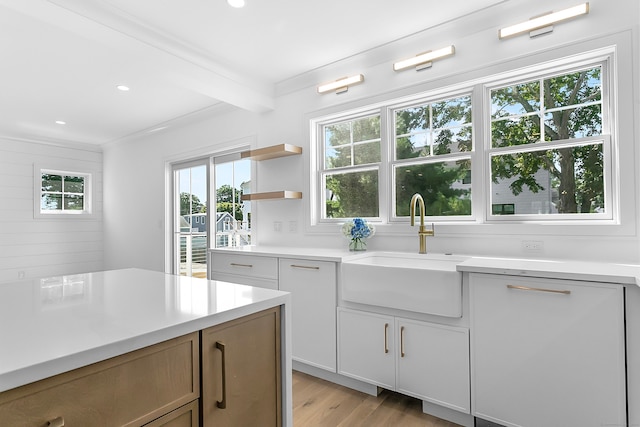 kitchen featuring sink, white cabinetry, ornamental molding, beamed ceiling, and light wood-type flooring