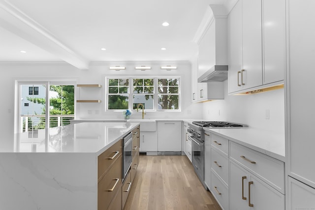 kitchen with wall chimney exhaust hood, sink, high end stainless steel range oven, light hardwood / wood-style floors, and white cabinets