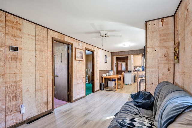 unfurnished living room with ceiling fan, light wood-type flooring, and wood walls