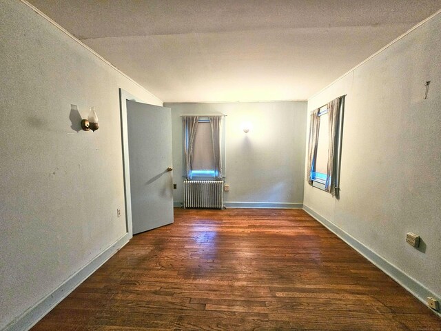 spare room with dark wood-type flooring, radiator heating unit, and ornamental molding