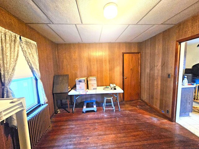 unfurnished office featuring radiator heating unit, dark hardwood / wood-style flooring, and wood walls