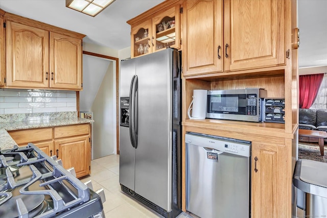 kitchen with stainless steel appliances, light stone countertops, light tile patterned floors, and backsplash