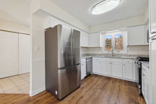 kitchen with light stone counters, appliances with stainless steel finishes, sink, and white cabinets