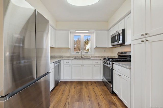 kitchen with white cabinetry, appliances with stainless steel finishes, sink, and wood-type flooring