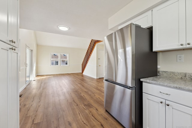 kitchen with white cabinetry, light stone counters, light hardwood / wood-style floors, and stainless steel refrigerator